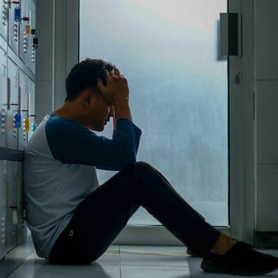 Мъж, седнал на пода до шкафчета, хванал главата си с ръка: изтощение от напрежение