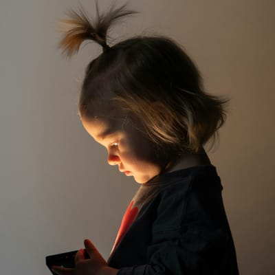 Малко дете с наведена глава, осветено от екрана на телефона